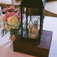 Black lantern centerpiece on a wooden box beside a pink-and-white floral arrangement