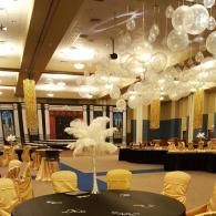 Decorated banquet hall with round tables, gold chairs, and white balloon decorations hanging from the ceiling