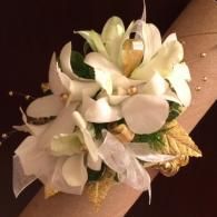 White flower corsage on a brown ribbon wristband against a dark background