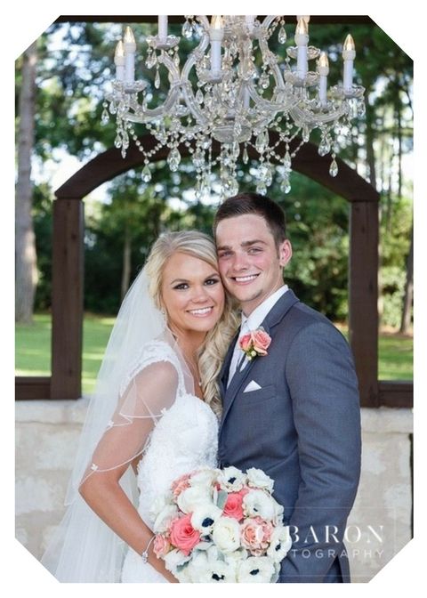 Bride and groom smiling under a chandelier, holding a bouquet in a garden pavilion.