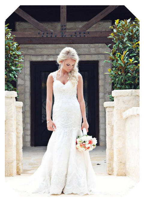 Bride in a white lace gown holding a bouquet, standing at a stone doorway.