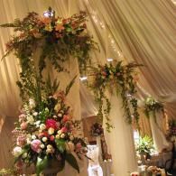 Elegant wedding venue with draped fabric, hanging floral arrangements, and a large pink-and-white bouquet.
