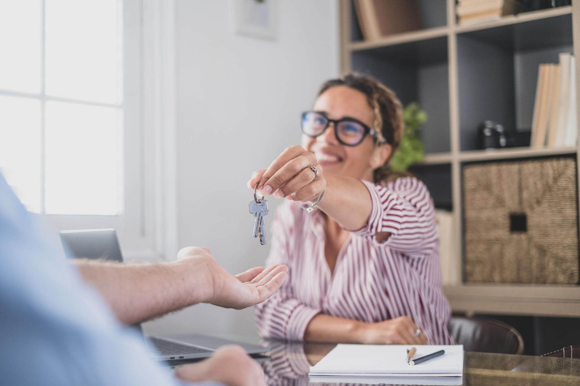 Woman in glasses hands over keys across a desk in a bright office