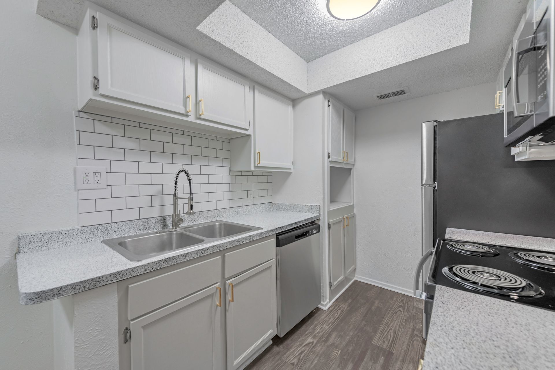 Modern kitchen with white cabinets, stainless steel appliances, and speckled countertops.