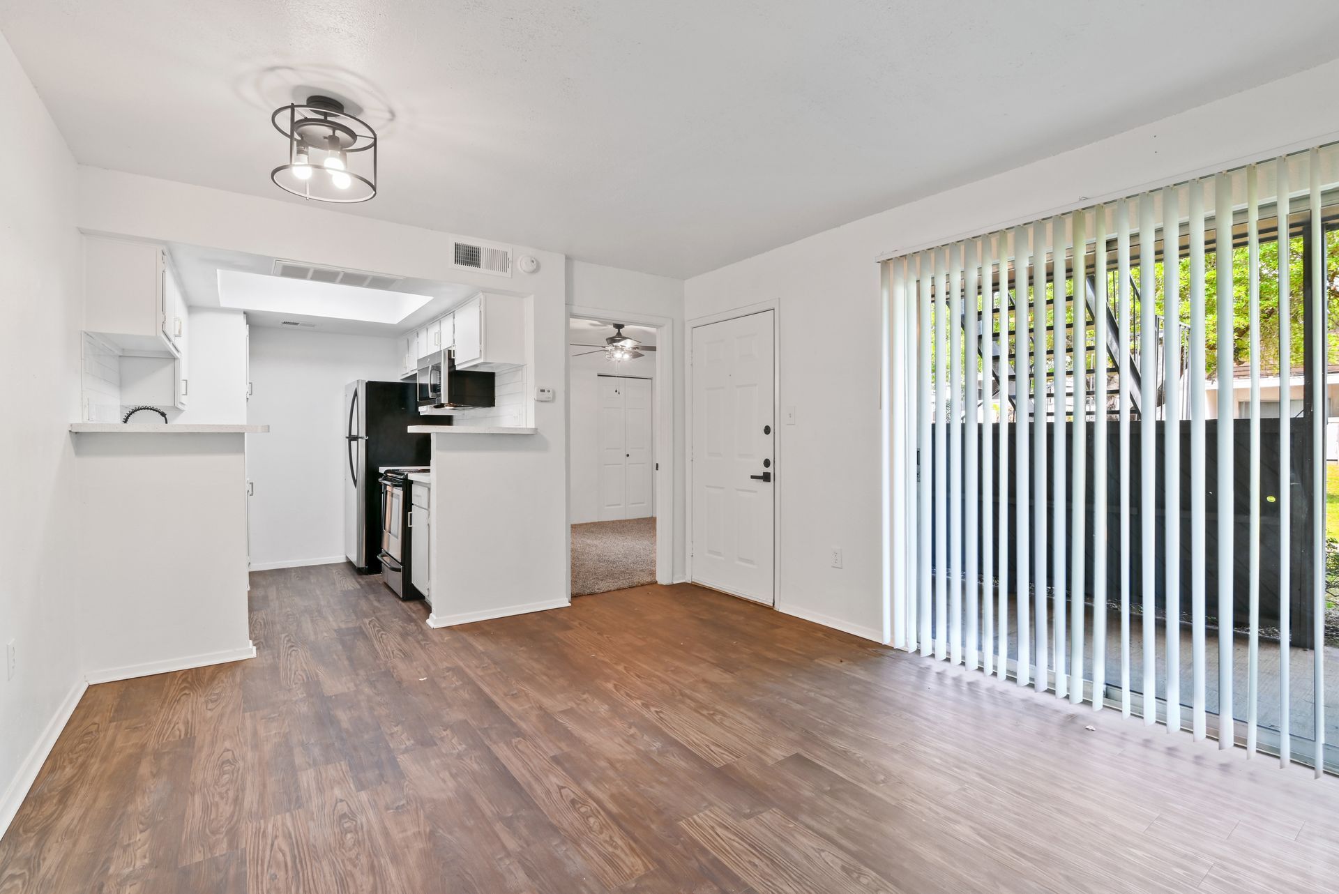 Bright living space with open kitchen, dark wood floor, and large sliding glass door.