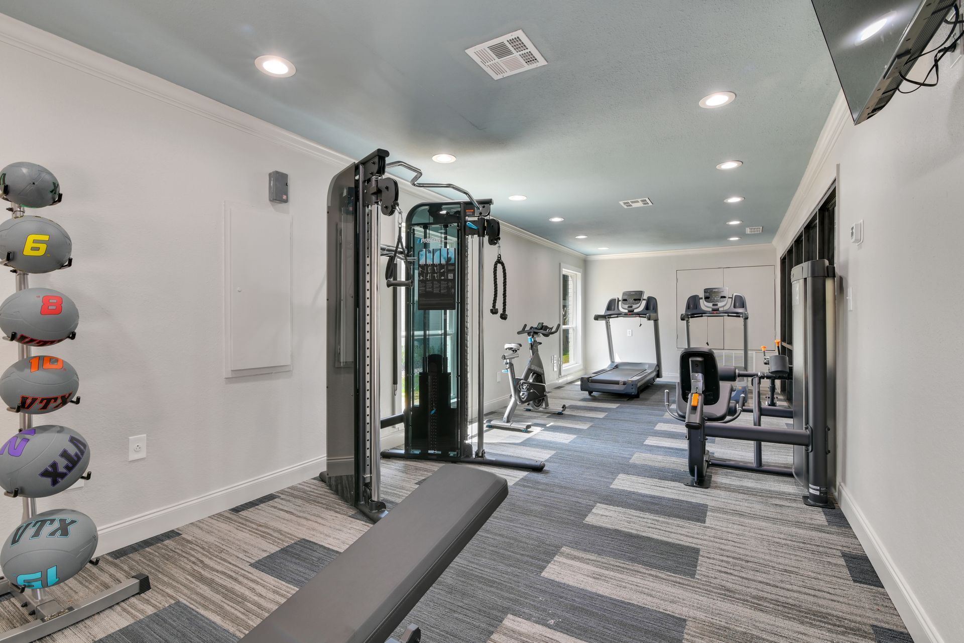 Gym with exercise equipment: weight rack, cable machine, treadmills.