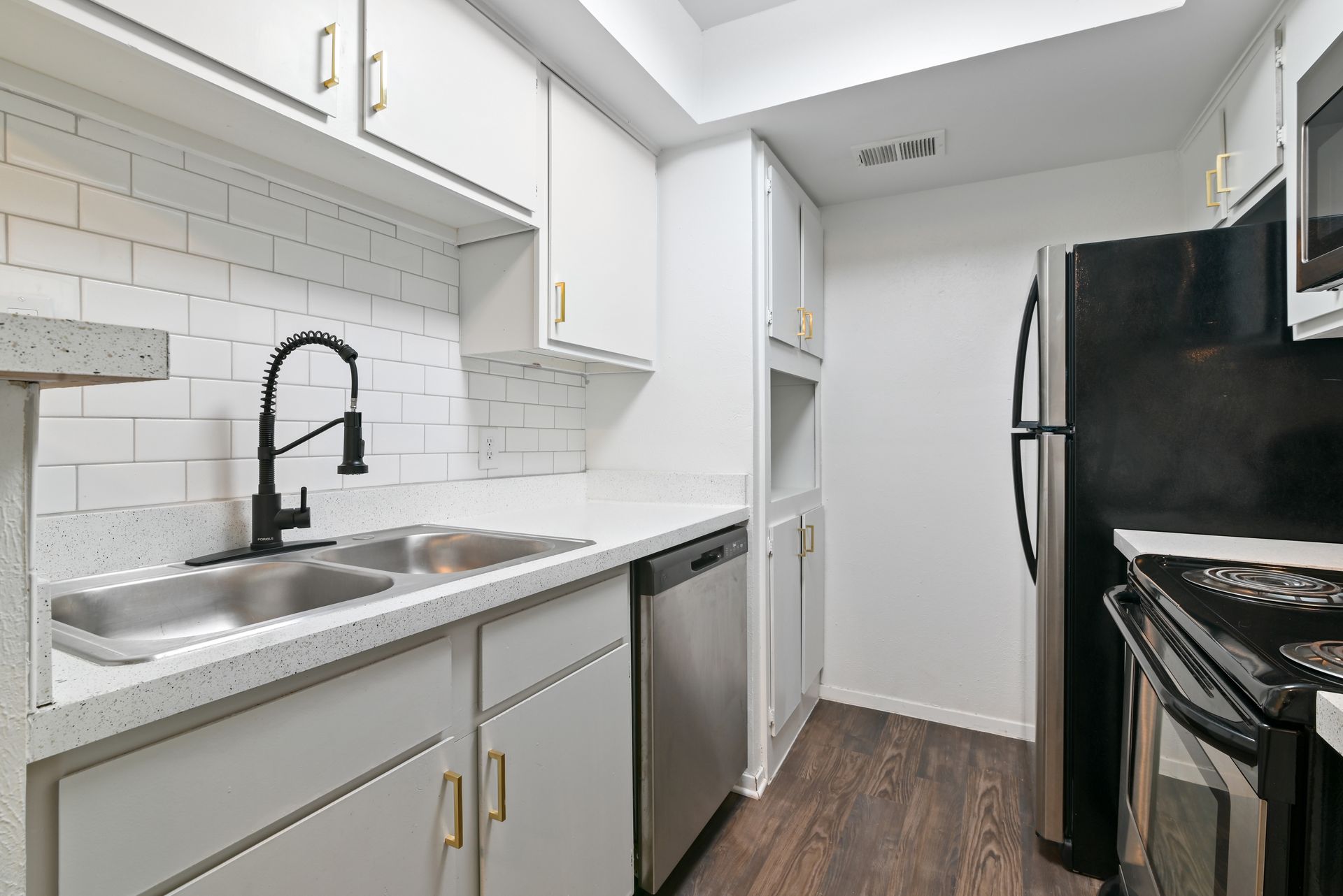 White kitchen with stainless steel appliances, gray cabinets, and black faucet.