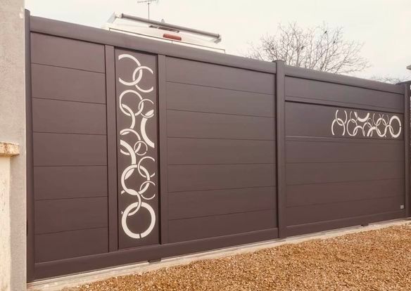 Portail coulissant motorisé en aluminium de Trihome Menuiseries. Le coulissant motorisé et son portillon sont dotés de motifs réalisés en découpe jet d’eau