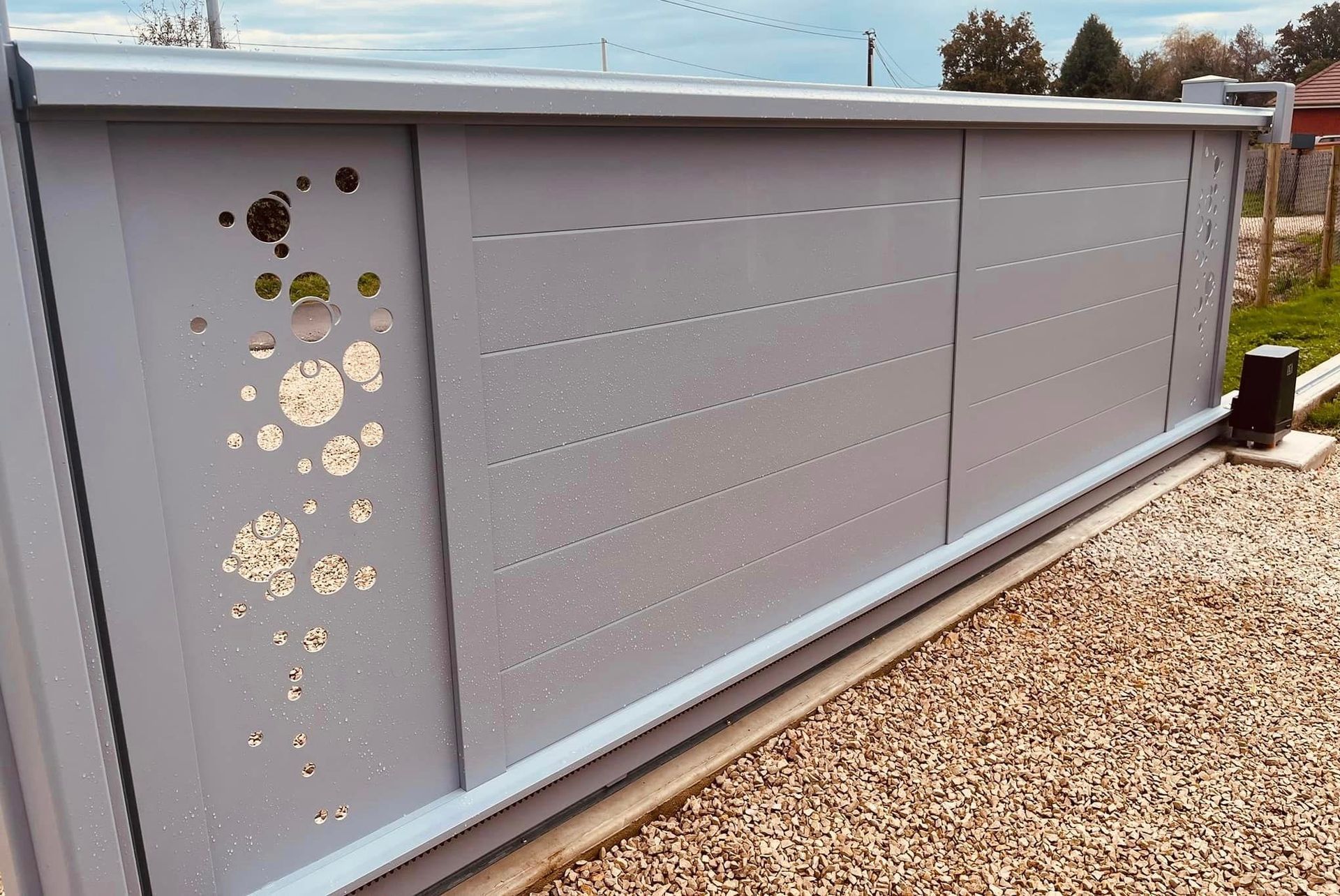 beau portail gris argent (ral 7040) en version coulissante sur rail motorisée, du modèle graffity steel Art et Portails avec motifs bulles latéraux