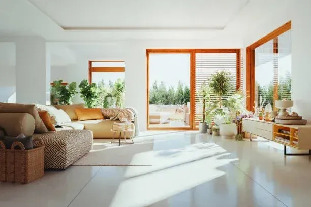Bright modern living room with beige sofa, plants, large windows, and sunlight on white floor
