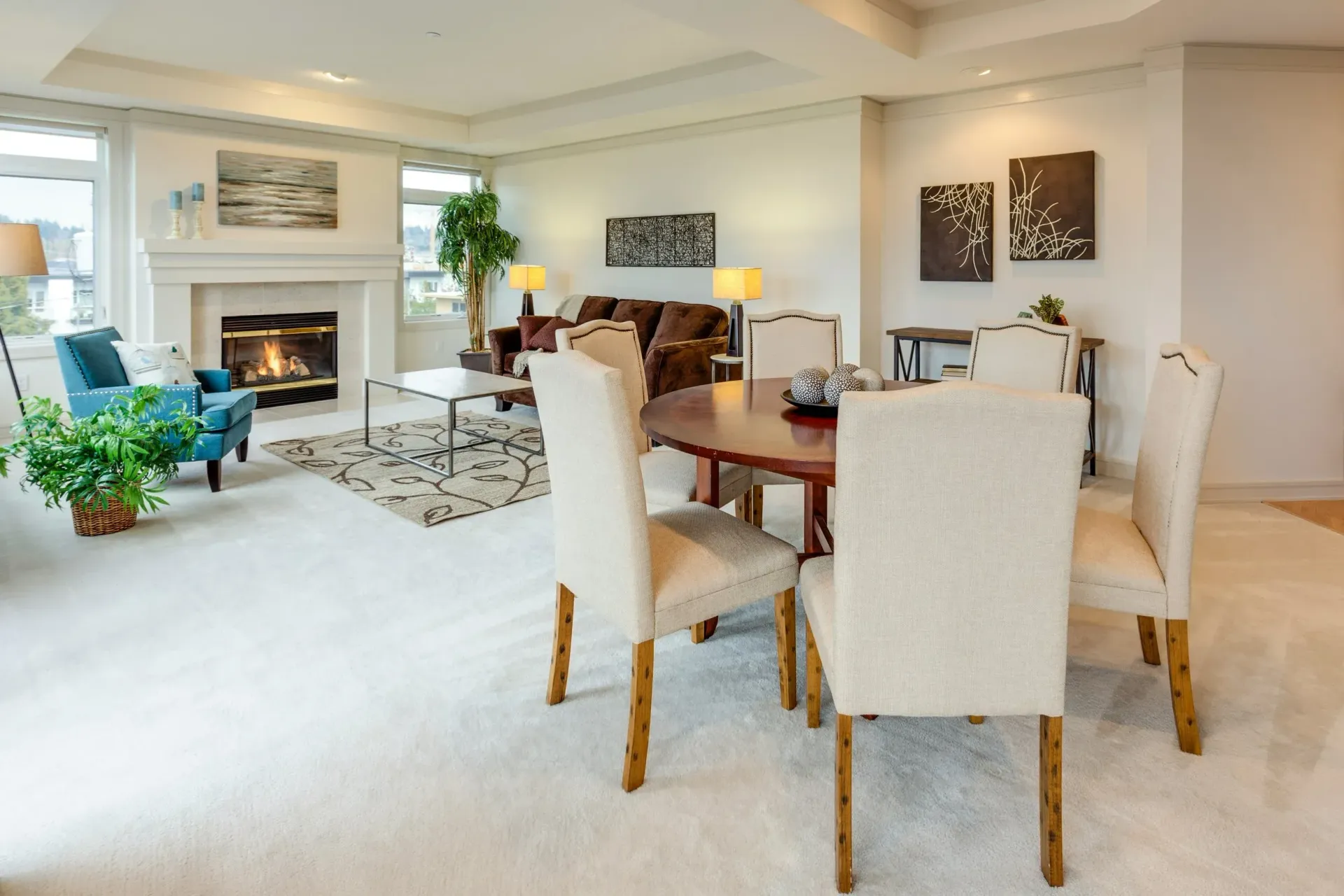 Bright living and dining room with white chairs, fireplace, plant, and wall art