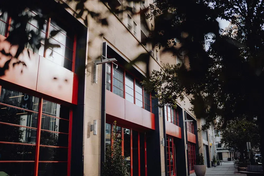Modern storefronts with red-trimmed windows under trees on a quiet street