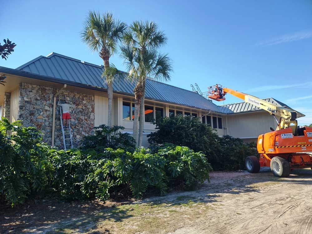 Orange crane truck lifting near a stone house with palm trees and blue sky