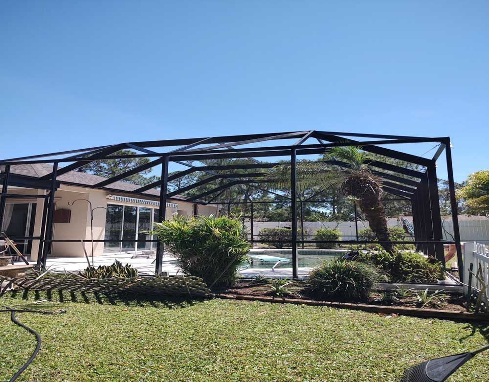 Collapsed black metal frame in a sunny yard beside a house and lawn, with trees and blue sky