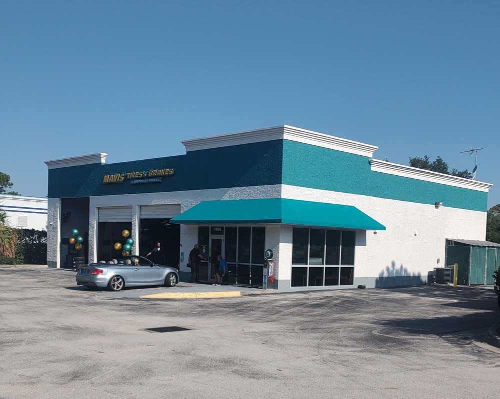 Low white-and-teal commercial building with a car parked outside on a sunny day