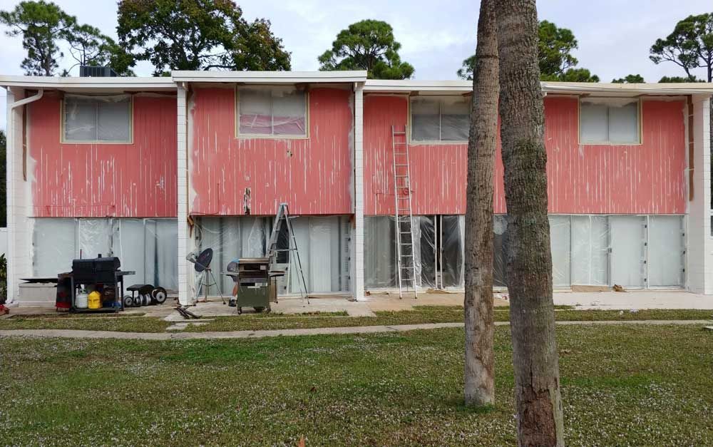 Two-story red and white apartment building with two palm trees in front, seen across a grassy yard