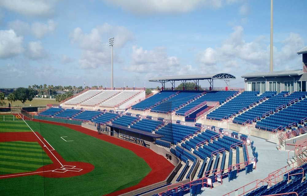 Empty baseball stadium with blue and white bleachers beside a red track and green field