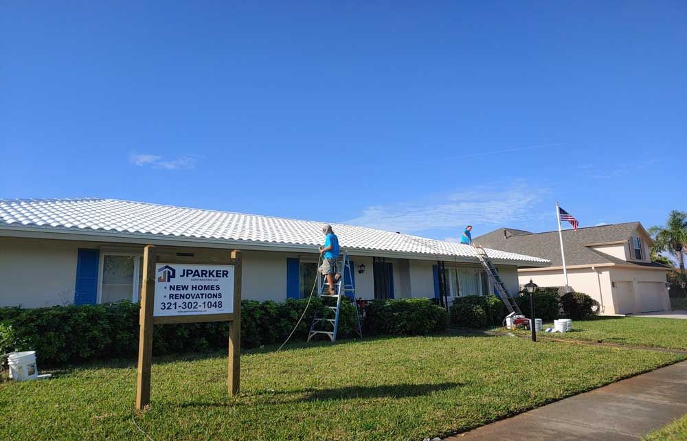 Single-story office building with a sign, blue sky, and workers on ladders near the entrance