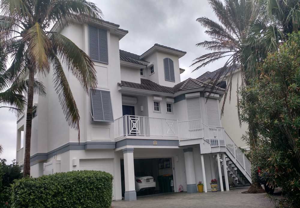Three-story white house with a garage, palm trees, and a staircase on the right