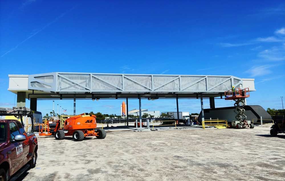 Industrial site with a long gray conveyor bridge, orange lift, and truck under a bright blue sky