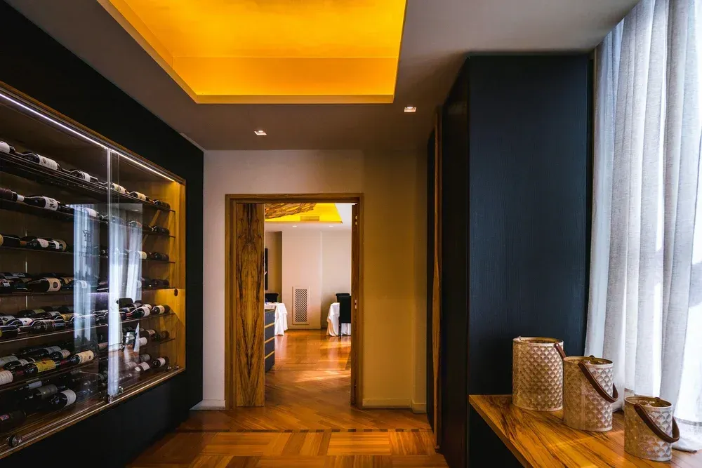 Modern wine cellar hallway with backlit shelves, dark walls, and wicker baskets on a wooden console.