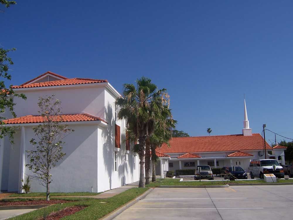 White building with red-tiled roof beside a church-like structure under a clear blue sky