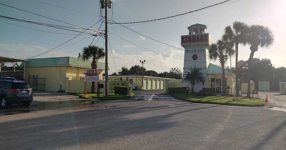 Clock tower and low buildings at a sunny street corner with palm trees and parked cars
