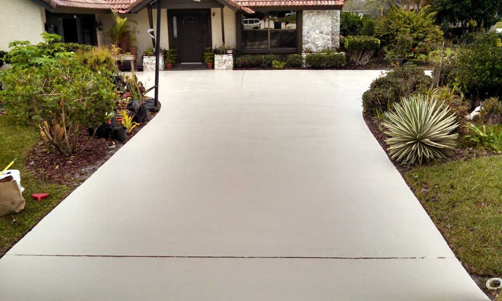 Freshly poured concrete driveway leading to a house with landscaped garden beds.