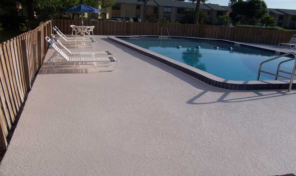 Outdoor pool with lounge chairs on a sunlit deck beside a wooden fence