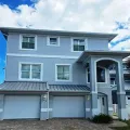 Two-story gray house with white trim, garage, front porch, and blue sky overhead