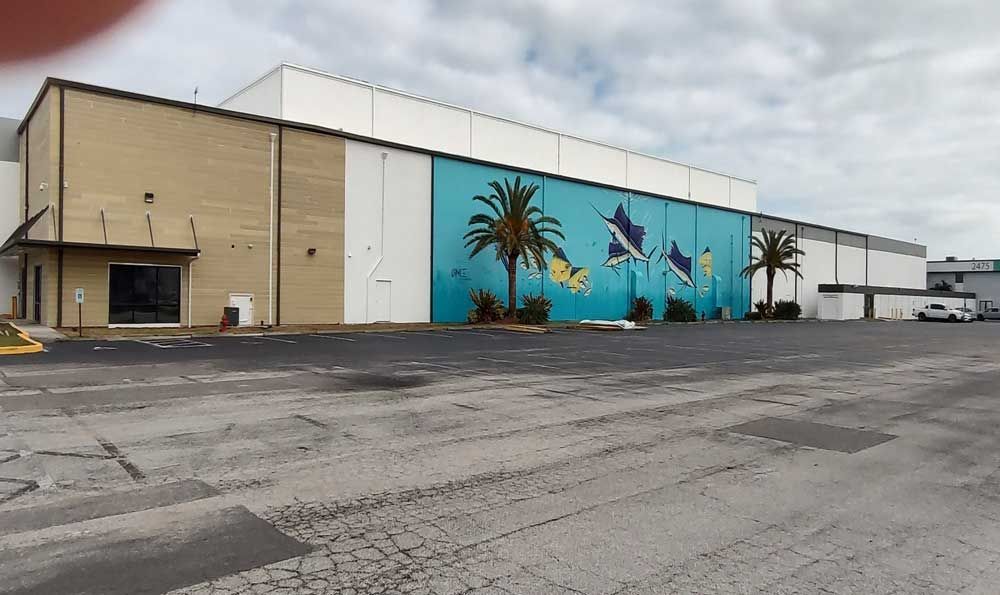 Industrial building with a large turquoise palm tree mural in an empty parking lot