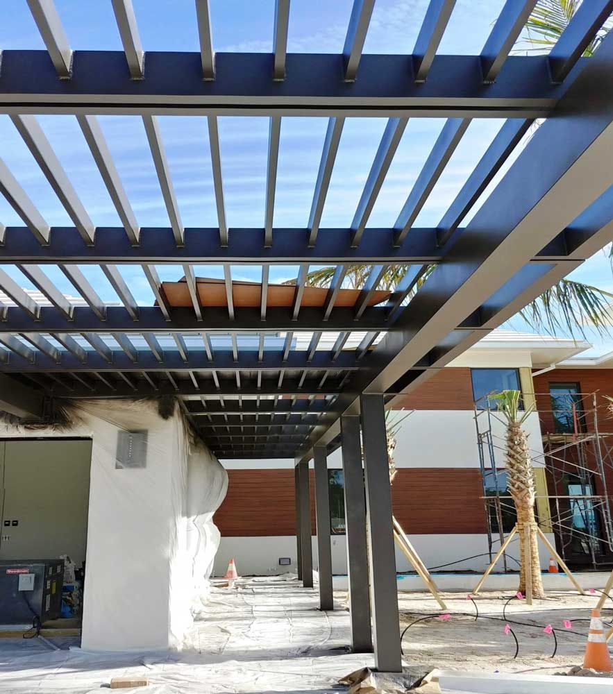 Covered outdoor walkway with black metal beams and white walls under construction