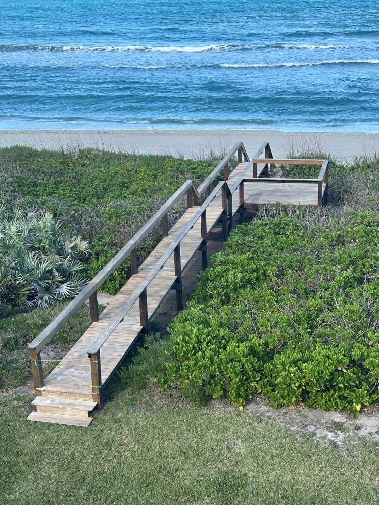 Wooden boardwalk stairway through dunes to a sandy beach with blue ocean beyond