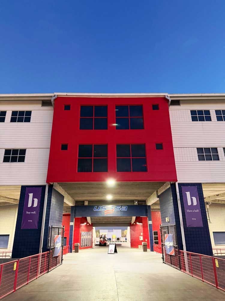 Front entrance of a building with a red central façade, white sides, and a lit walkway at night