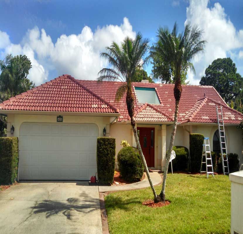 Single-story house with red tile roof, white garage, palm trees, and a ladder in the front yard.