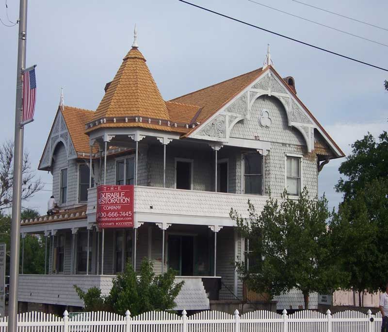 Victorian-style white house with a pointed orange roof and porch, behind a white picket fence.