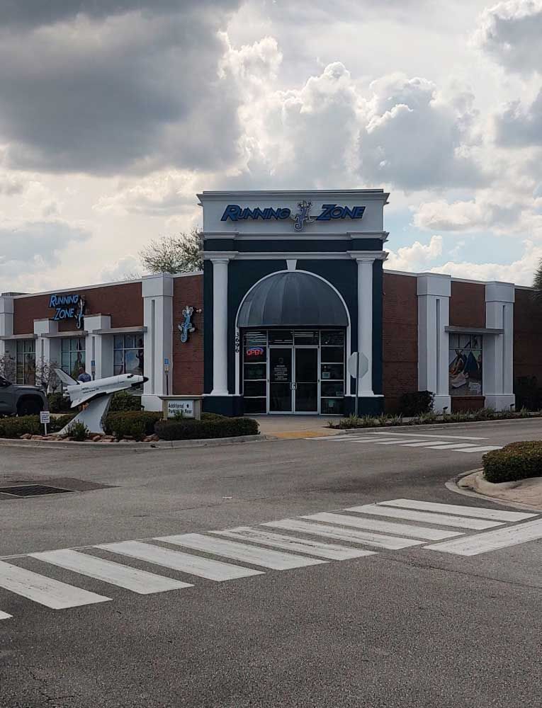 Empty storefront with an arched entrance and clouded sky, viewed across a striped crosswalk.