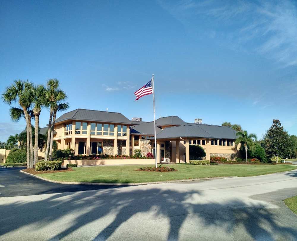 Large tan building with a U.S. flag, palm trees, and a circular driveway under a clear blue sky