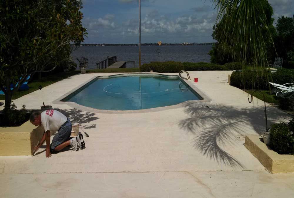 Man cleaning a poolside patio beside a blue swimming pool overlooking the water