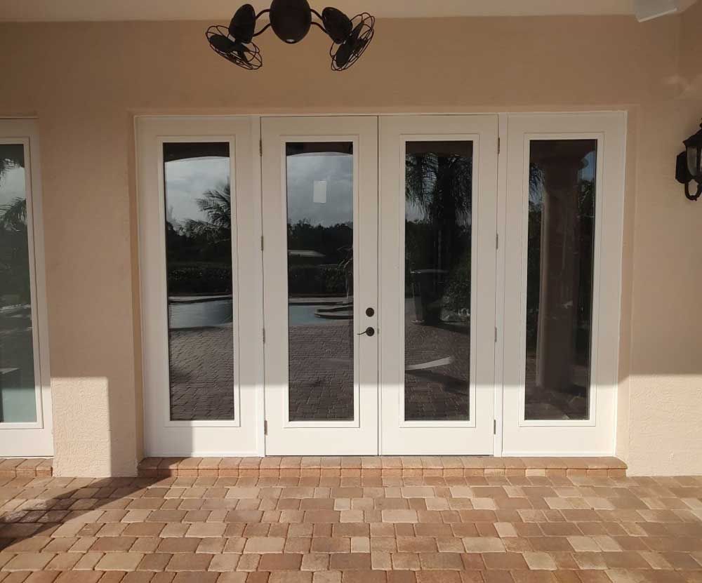 White double front doors with glass panels beneath a covered patio over brick paving.