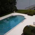 Poolside deck with turquoise water, white patio, trimmed hedges, and a railing overlooking the water