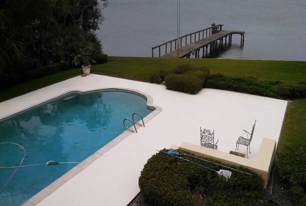 Backyard pool beside a lawn and dock on a lake, with white patio and chairs