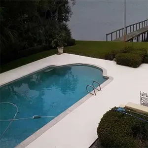 Poolside deck with turquoise water, white patio, trimmed hedges, and a railing overlooking the water