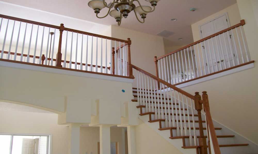 Interior view of a home foyer with a staircase, white railings, and a chandelier above.