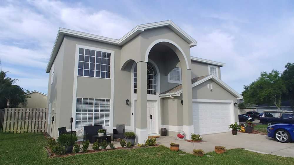 Two-story beige house with white trim, arched entry, garage, and a lawn under a cloudy sky