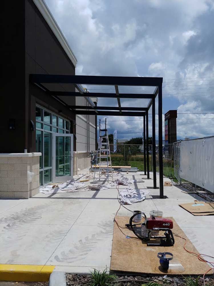 Partially built covered walkway beside a building, with construction materials and tools on the ground under cloudy skies.