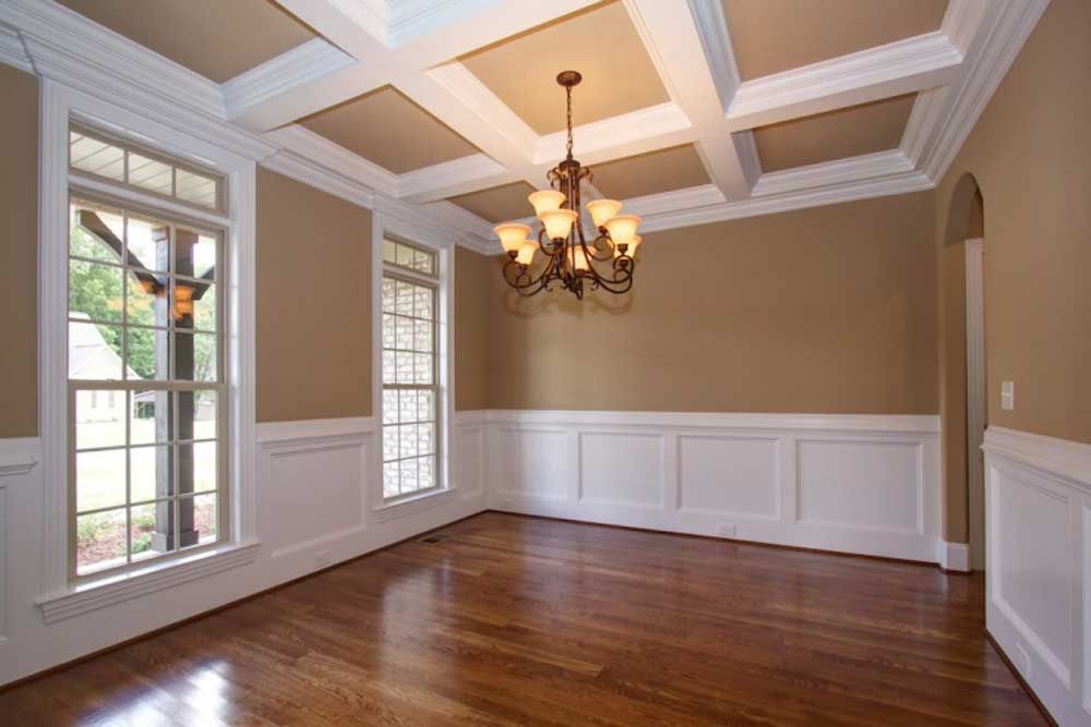 Empty formal dining room with hardwood floors, coffered ceiling, chandelier, and tall windows