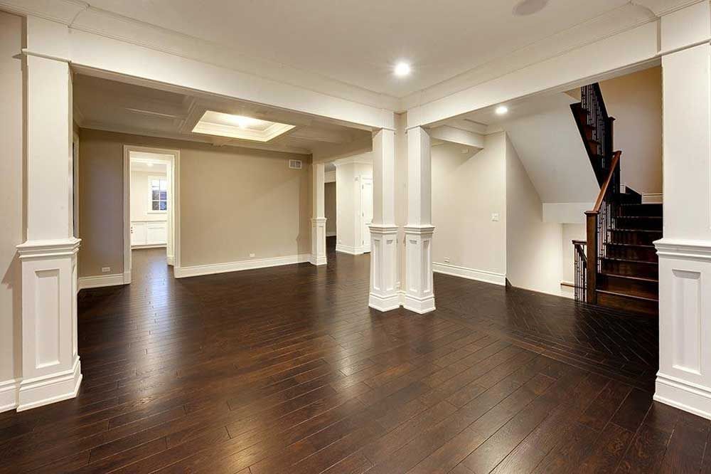 Empty modern room with dark hardwood floors, white trim, and a staircase on the right.