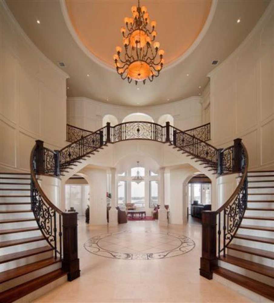 Grand foyer with twin curved staircases, ornate chandelier, and polished marble floor