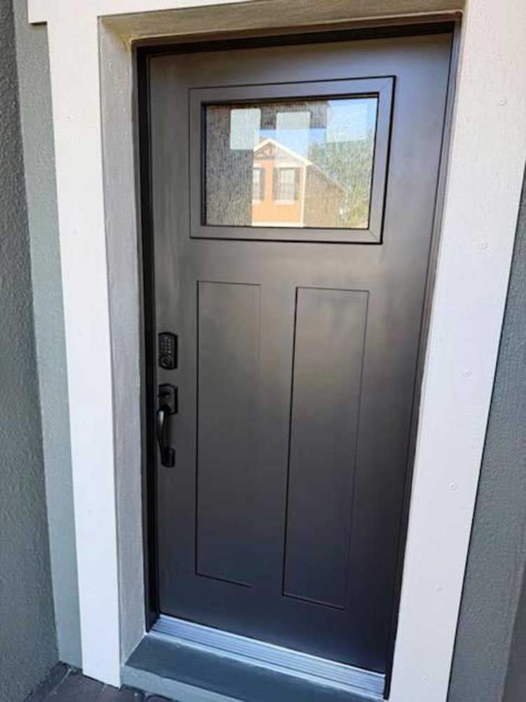 Dark gray front door with a small window and black handle in a white entryway.